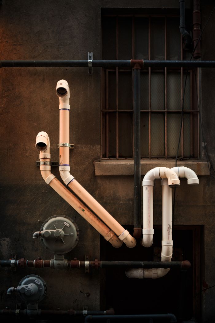 Services-01 Vertical shot of industrial pipes on urban building wall, showcasing intricate installation.