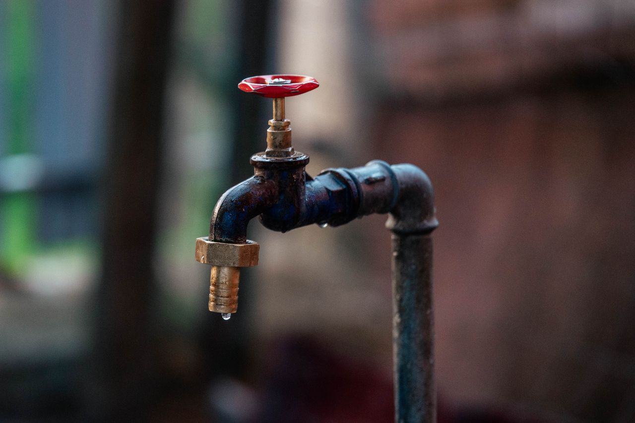 creative-01 Close-up of a rusty outdoor water faucet with a single droplet falling from the spout.