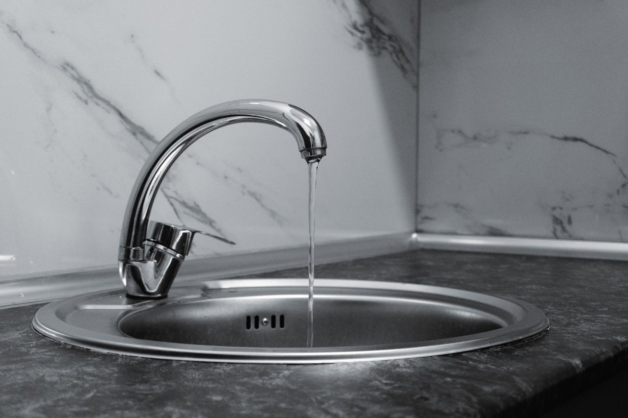 Services-02 Chrome faucet with running water in a modern kitchen with marble countertop.
