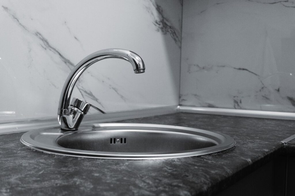 pexels-photo-34295403 Stainless steel kitchen sink and faucet against marble backsplash in a modern kitchen.