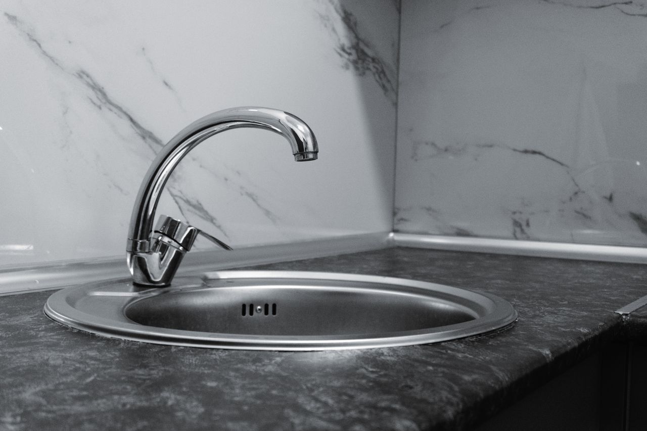 Stainless steel kitchen sink and faucet against marble backsplash in a modern kitchen.