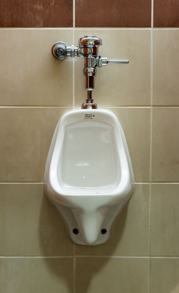 brand-02 Close-up view of a wall-mounted urinal in a public restroom, showcasing plumbing fixture.