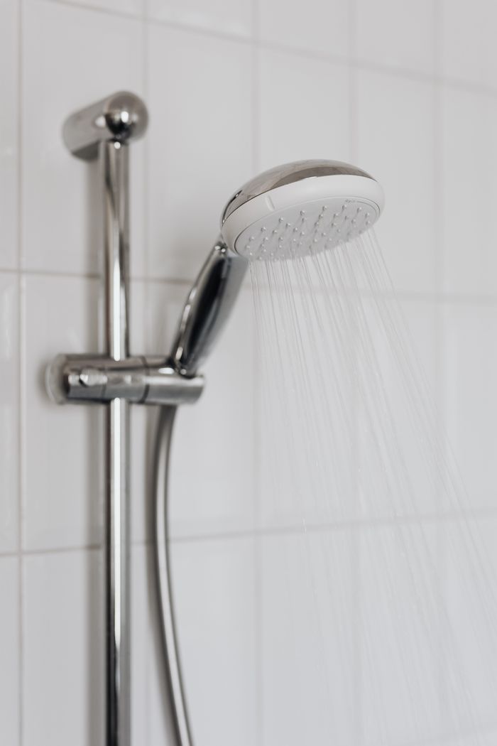brand-01 Close-up of a chrome shower head with water flowing, showcasing sleek modern bathroom design.