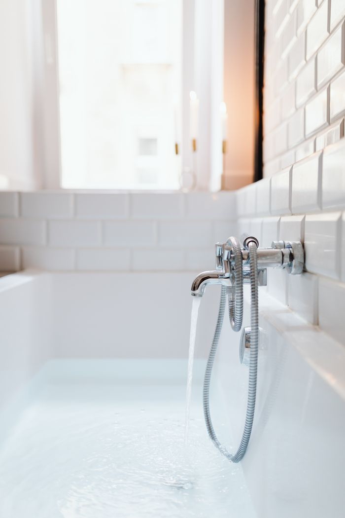 creative A modern white bathtub with chrome faucet and running water in a stylish tiled bathroom.